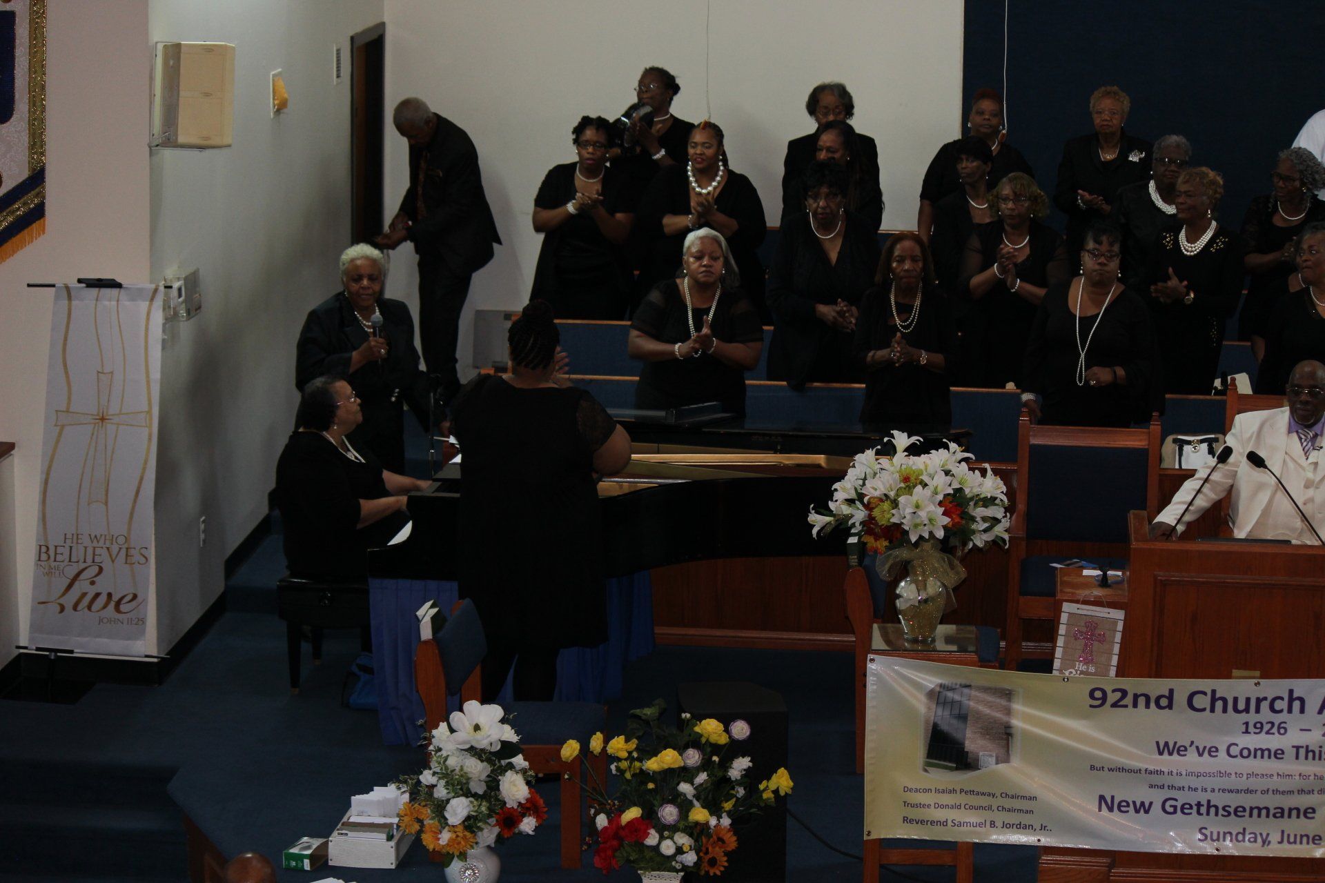 Choir standing in church sanctuary during a service, with pulpit and floral arrangements in front