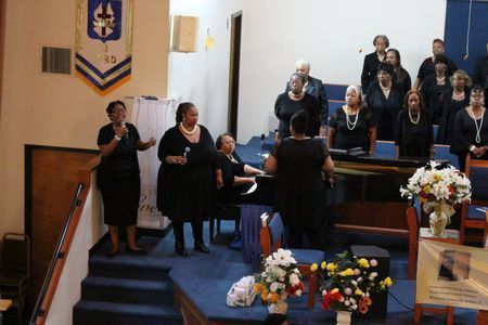 Choir singing in a church sanctuary with a conductor and floral arrangements at the front