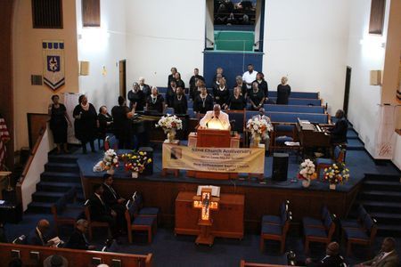 Church service with congregation seated in pews and choir behind a flower-adorned altar