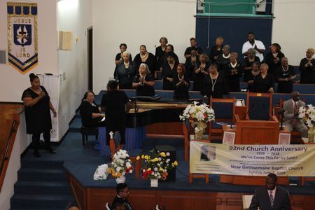 Church choir performing on a blue-carpeted stage with piano, flowers, and a 72nd anniversary banner