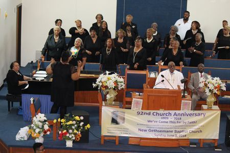 Choir singing on church stage beside banners and flower arrangements at a church anniversary service