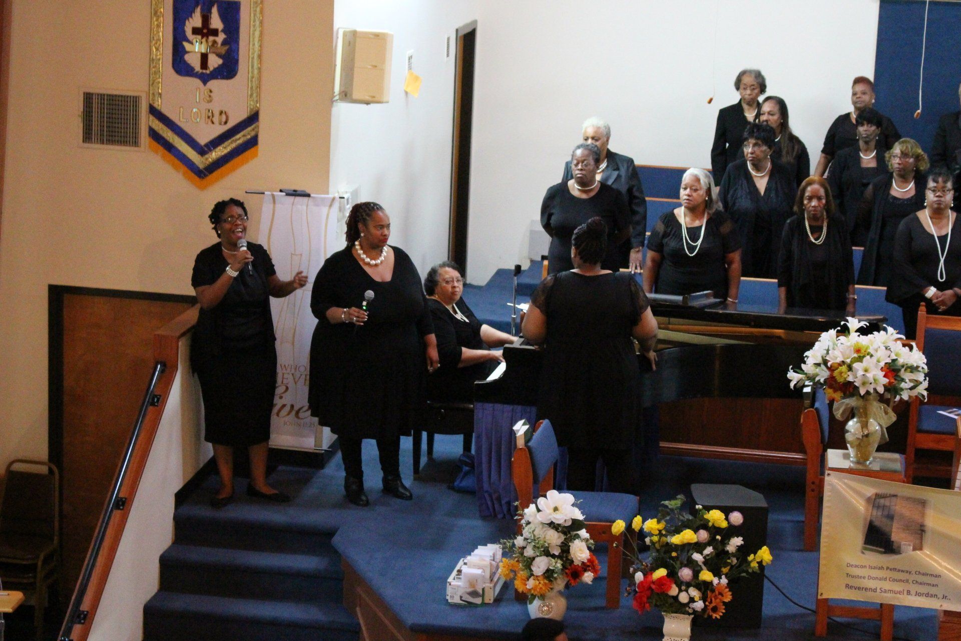 Choir singing in a church sanctuary near a pulpit decorated with flowers and a flag
