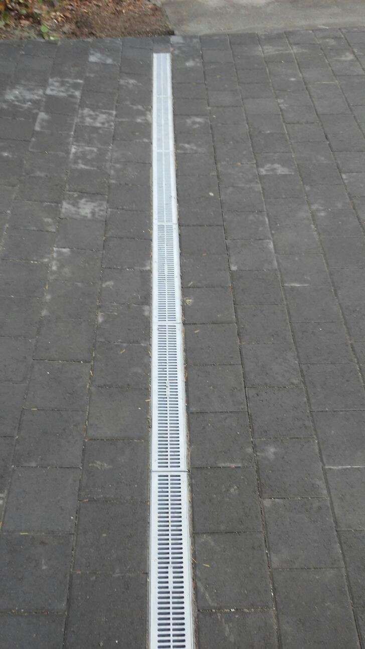 Sidewalk with a long white drainage grate running down the center of gray paving stones.