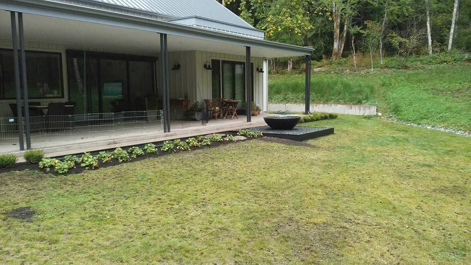 Modern house with a covered patio, lawn, and wooded yard.