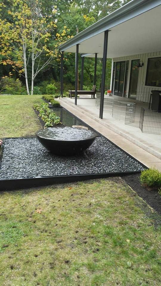 Backyard patio with a large black bowl fountain on a gravel platform beside a covered porch.