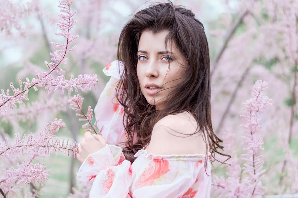 A woman in a white dress is standing in front of a cherry blossom tree.