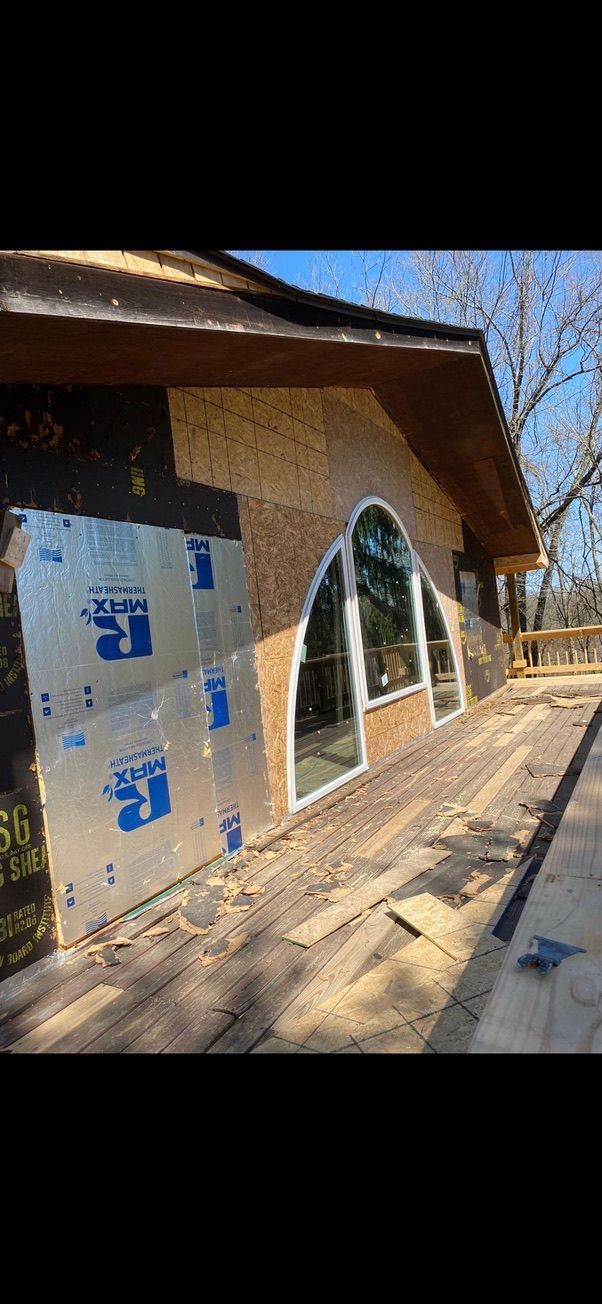 House under construction with blue insulation panels and arched windows, viewed along a wooden porch.