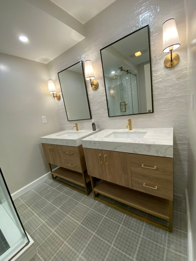 Modern bathroom with double vanity, large mirrors, sconces, and gray tile floor