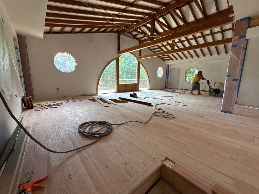 Partially renovated room with exposed beams, unfinished floor, and large arched windows