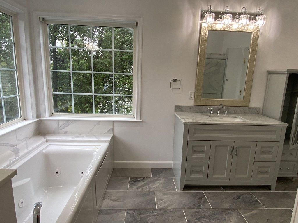 Bright bathroom with white tub, gray vanity, large window, and mirror above sink.