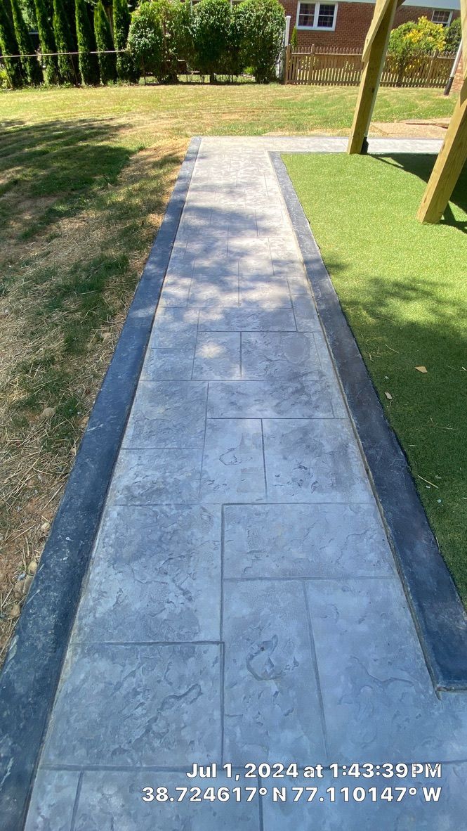 Concrete garden path bordered by grass, leading past trees and a house in the background