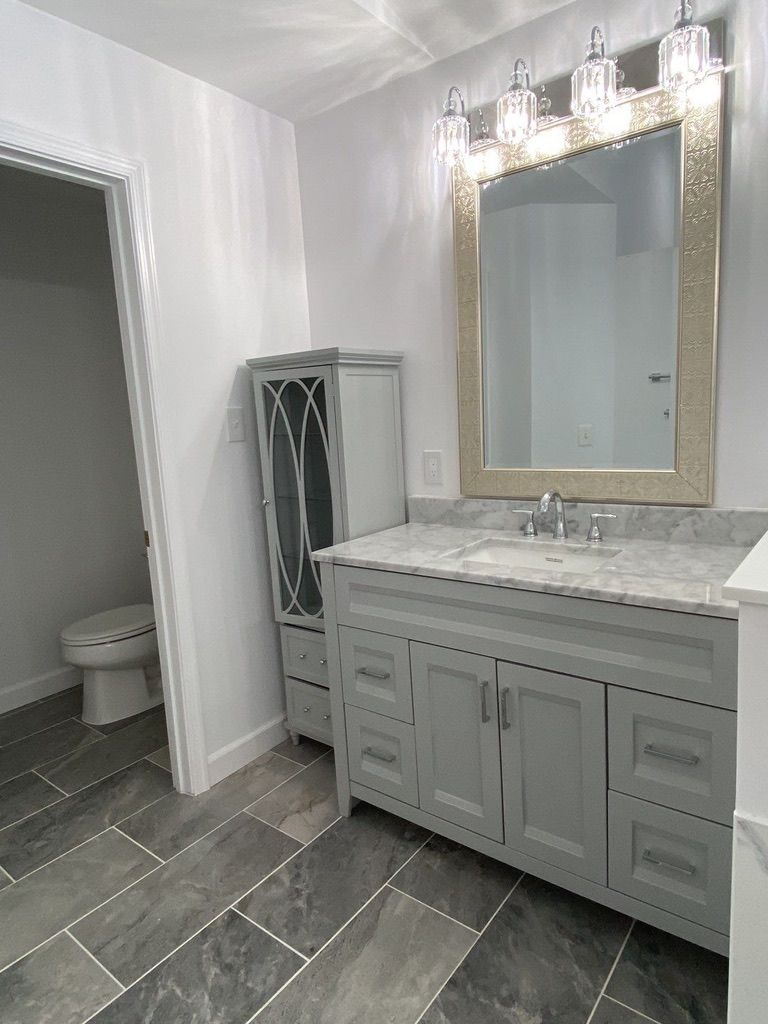 Gray bathroom vanity with marble countertop, large mirror, and open closet beside a toilet.