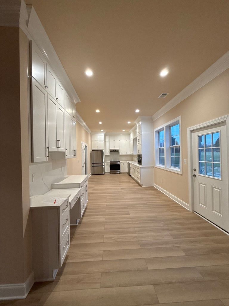 Bright hallway in a modern home with white cabinets, wood flooring, recessed lights, and a door at the end.