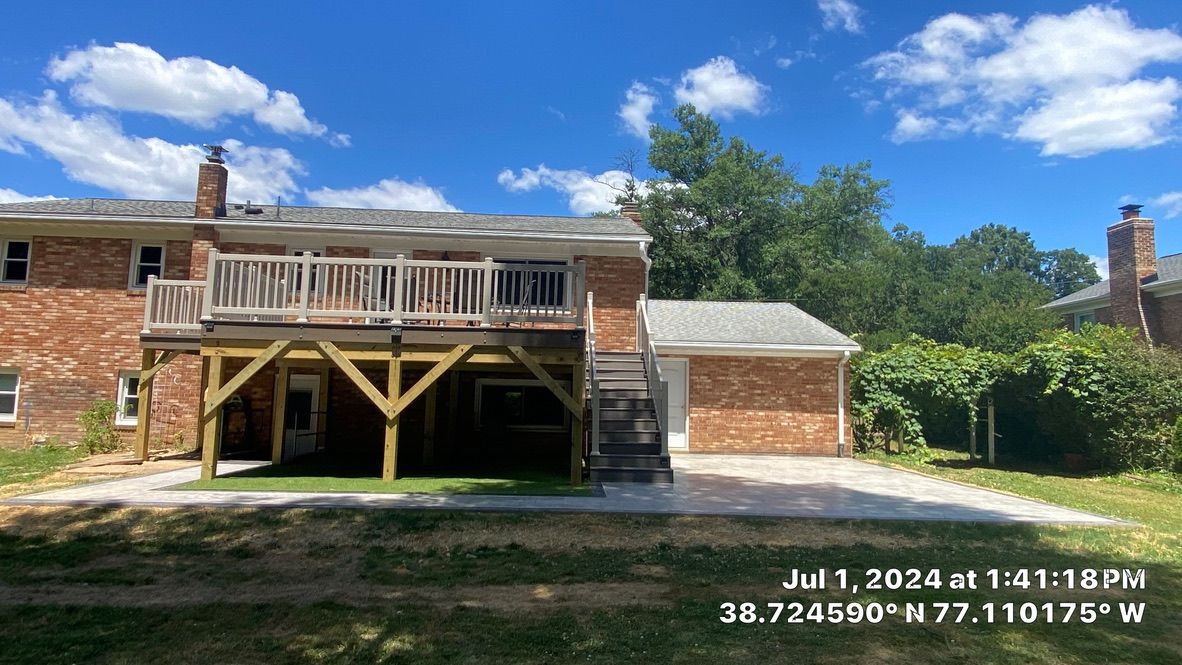 Brick house with wooden deck and carport under a blue sky, viewed from the backyard.