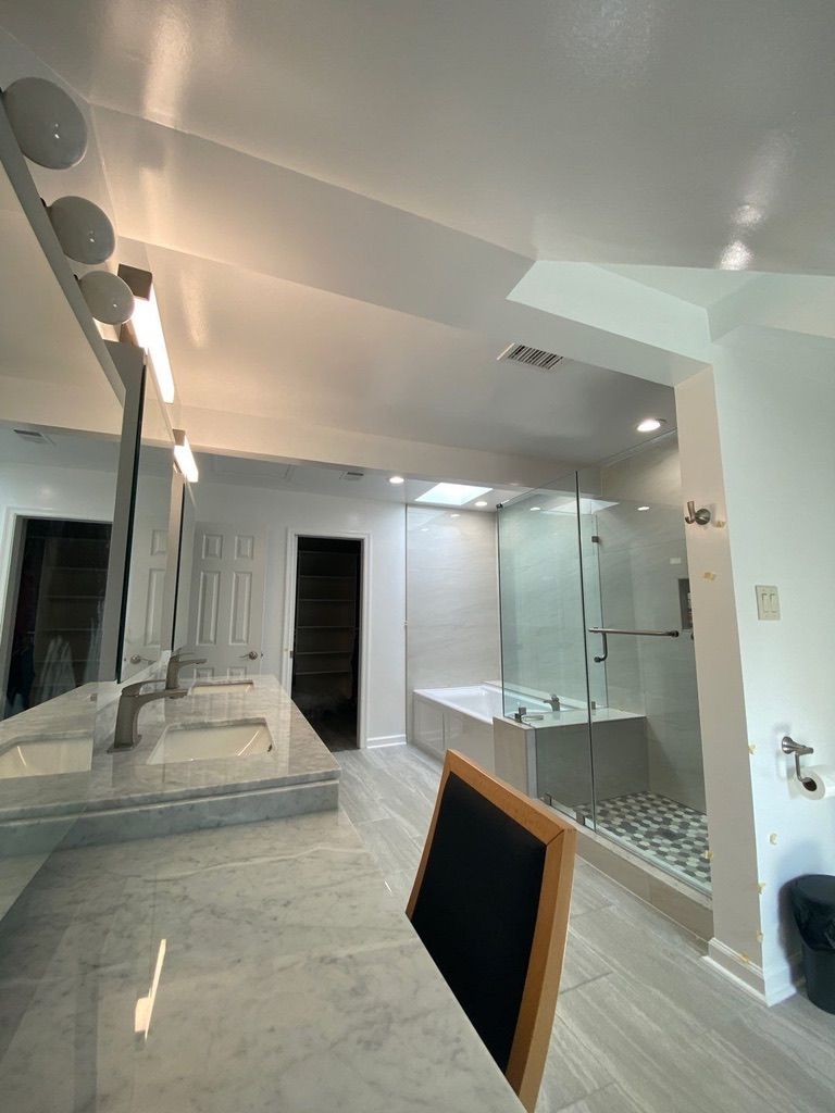 Bright bathroom with double vanity, large mirror, glass shower, and freestanding tub.