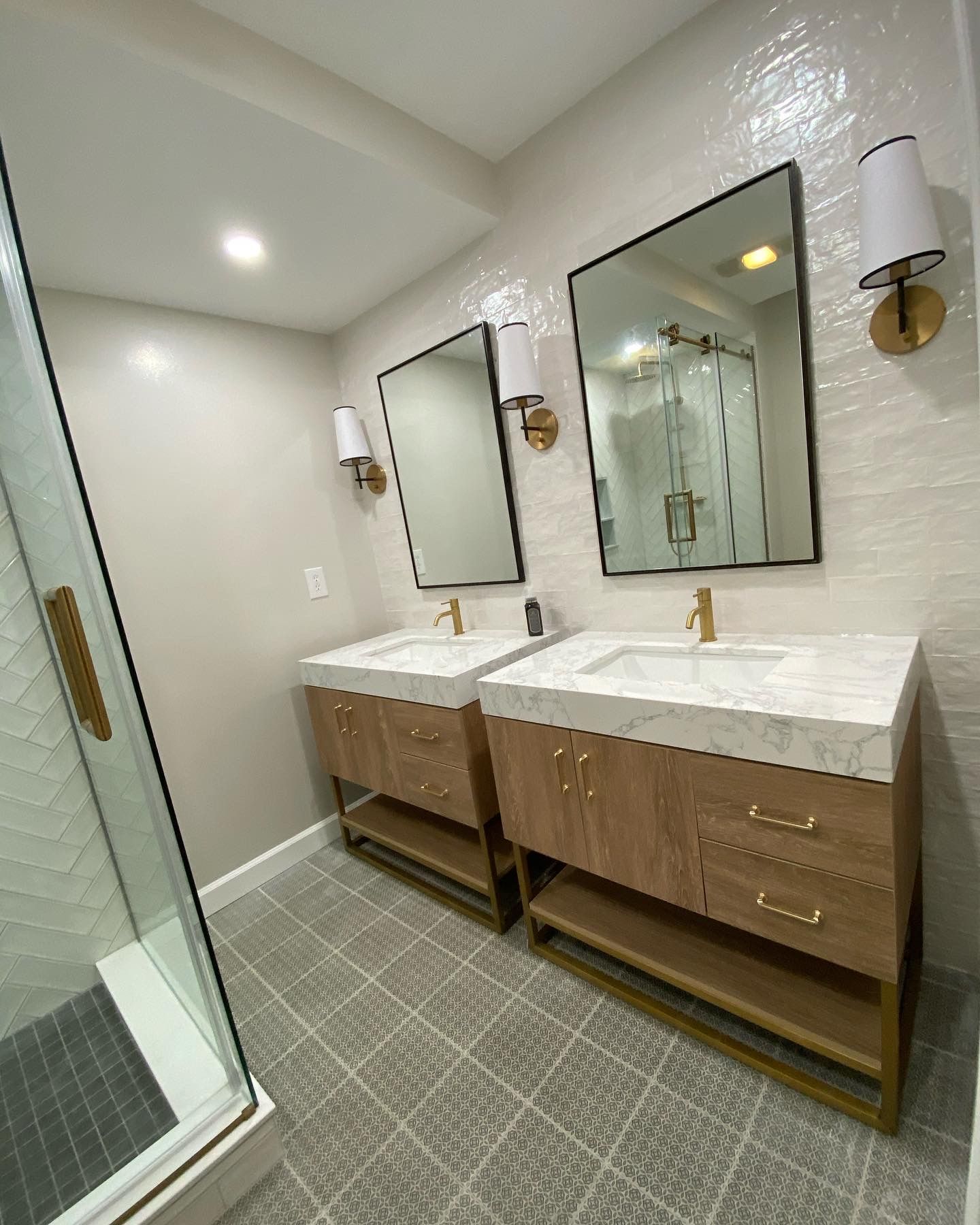 Modern bathroom with double wooden vanity, two mirrors, brass sconces, and tiled floor