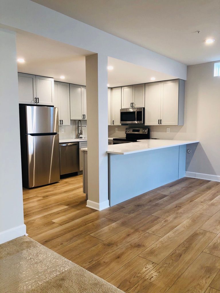 Empty kitchen with stainless steel appliances, white cabinets, and wood flooring in an open-plan room.