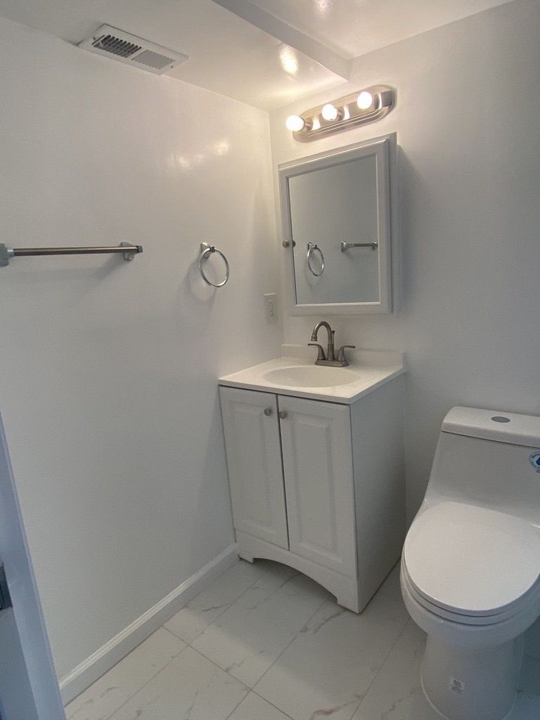 Small white bathroom with vanity, mirror, light fixture, towel bar, and toilet