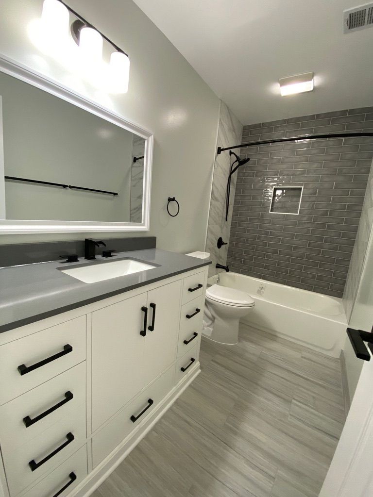 Modern bathroom with white vanity, large mirror, and tiled tub-shower area with gray accent wall.