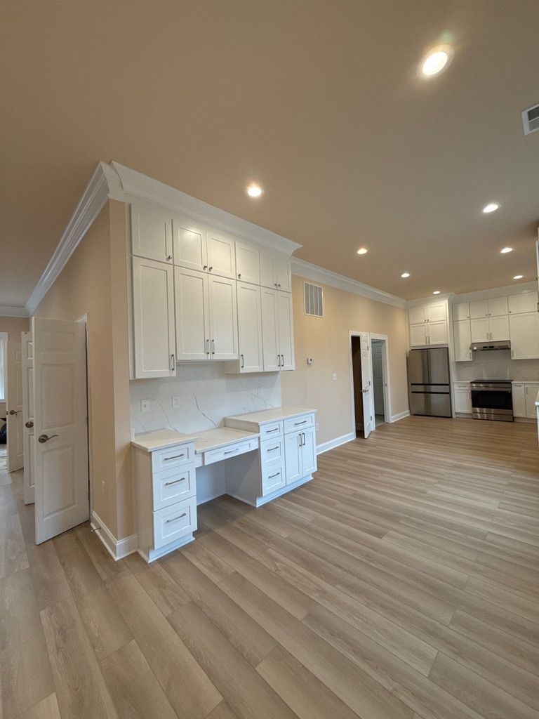 Bright open kitchen with white cabinets, wood floors, recessed lights, and a built-in desk area
