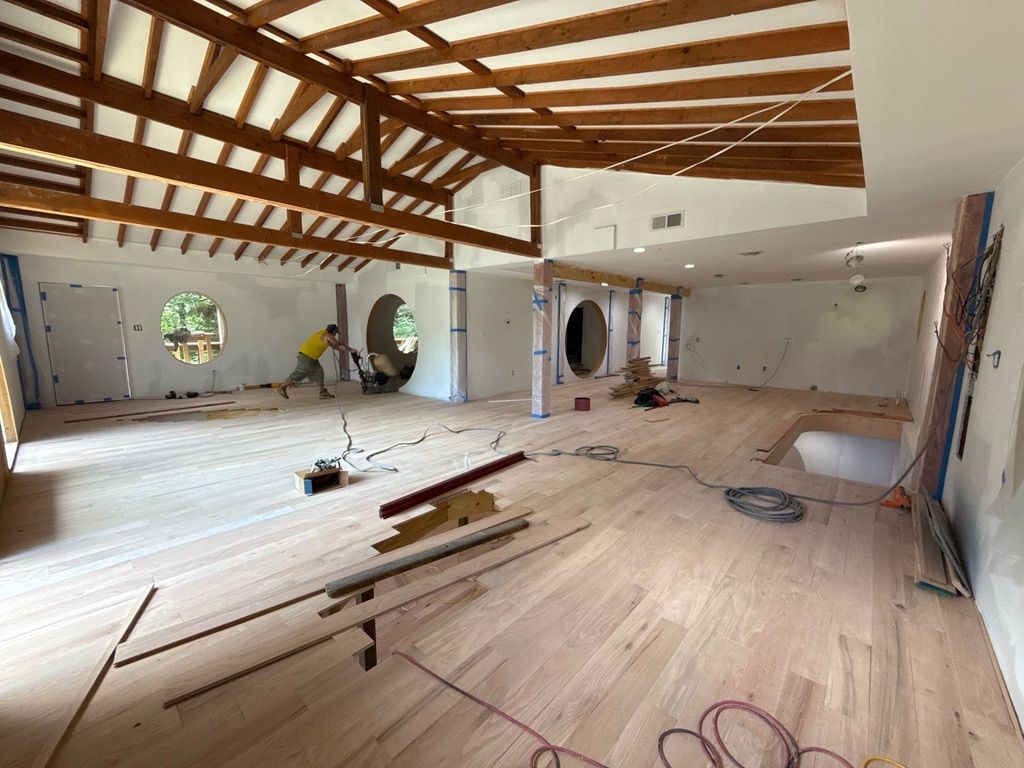 Renovated room with exposed wooden beams, white walls, and construction materials scattered across the floor.