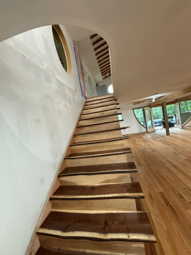 Modern interior staircase with wooden steps, white walls, and a bright open room with large windows