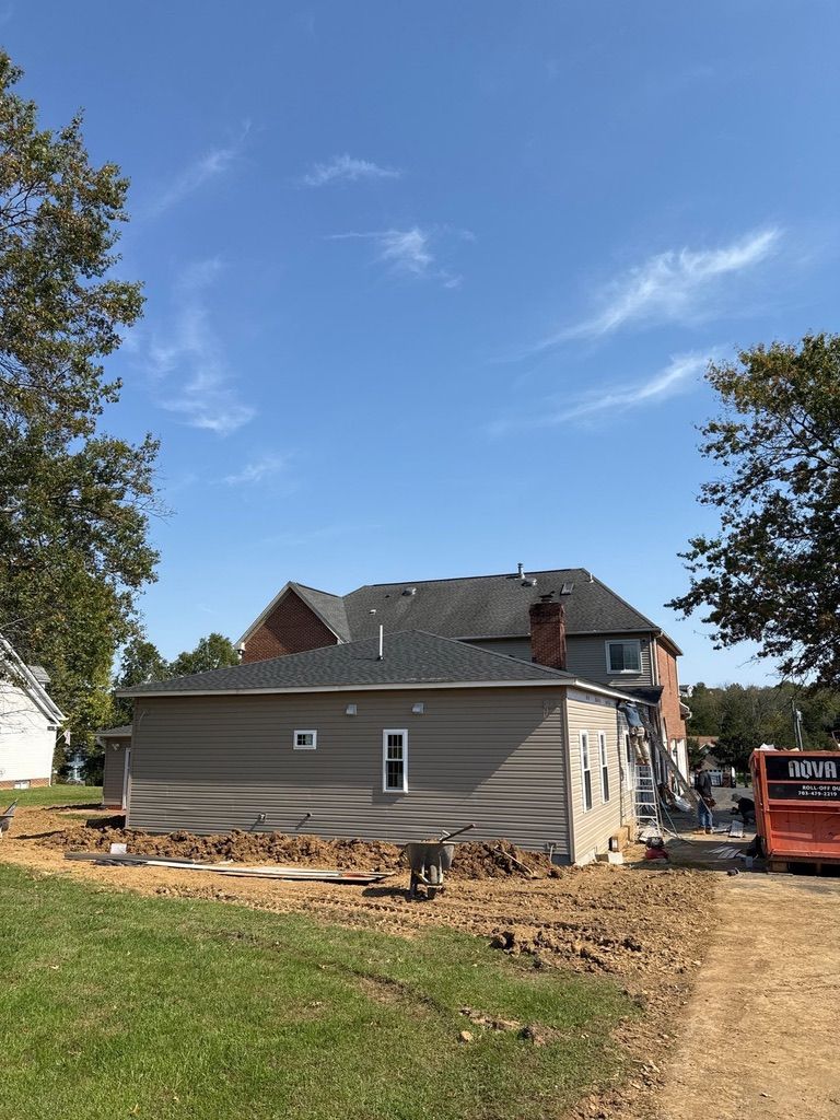 House under renovation with new tan siding, a partially damaged roof, and construction equipment outside.