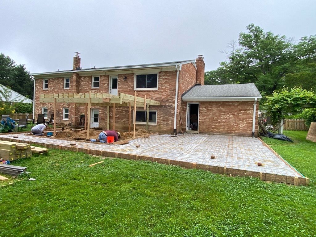 Brick house exterior with a paved patio and detached garage under construction, surrounded by a grassy yard.