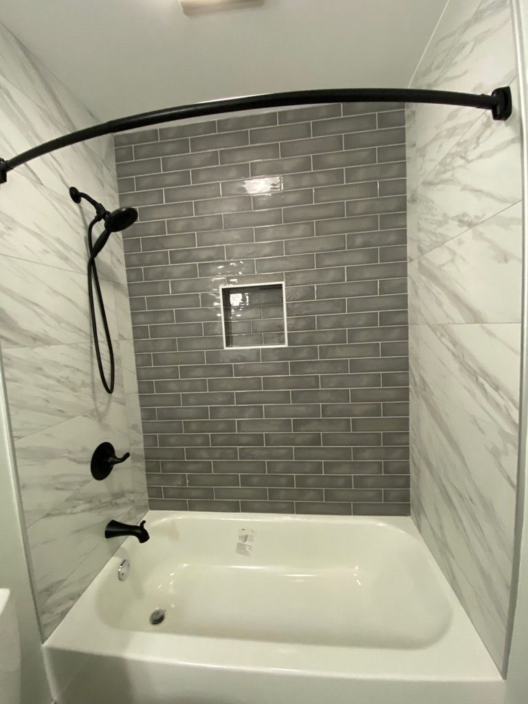 Bathroom tub and shower with gray tile accent wall, black shower fixtures, and white marble side walls