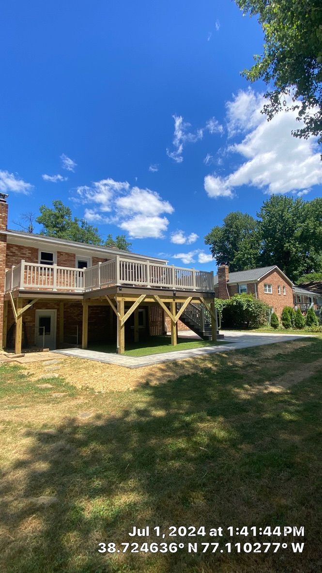 Two-story wooden house under construction on a sunny day, with blue sky and trees nearby