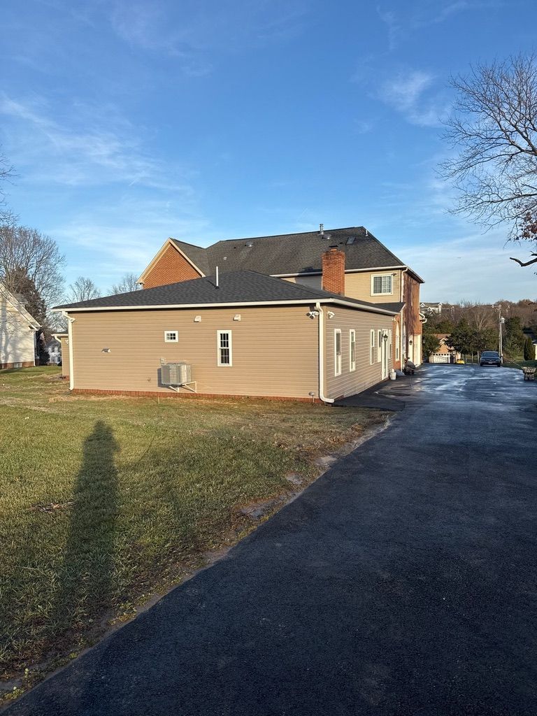 Tan house with white trim beside a driveway under a blue sky, viewed from the lawn