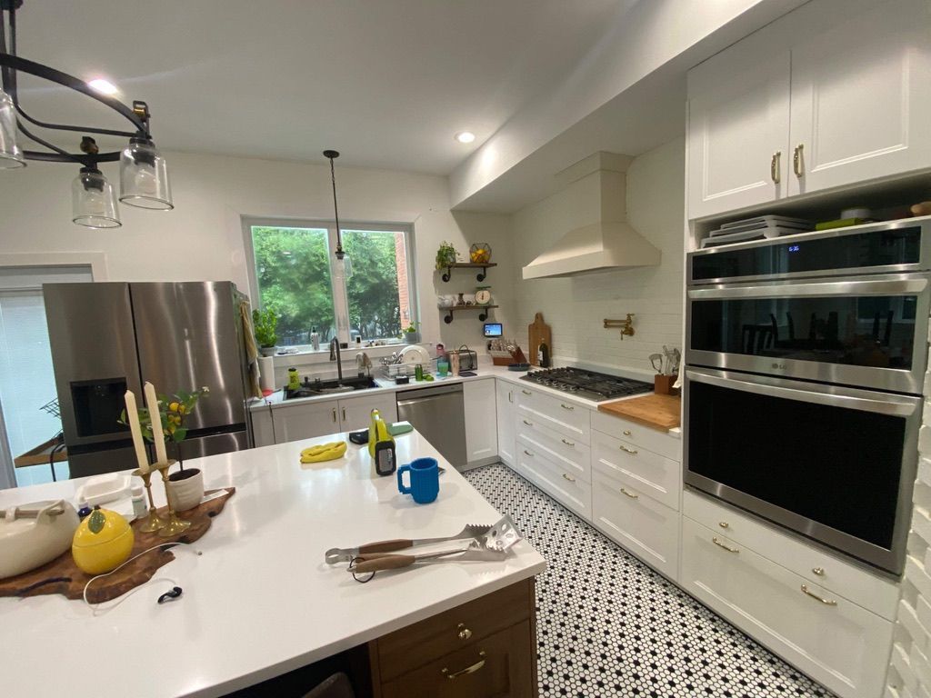 Bright white kitchen with island, stainless steel fridge, built-in oven, and window over the sink