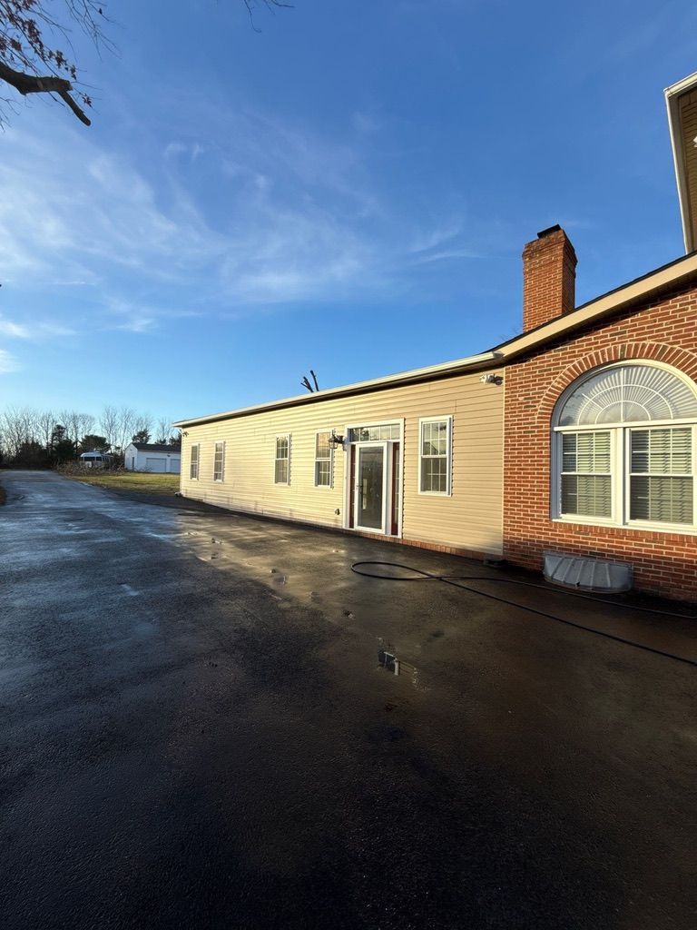 Single-story beige building with brick chimney beside a wet paved driveway under a blue sky.