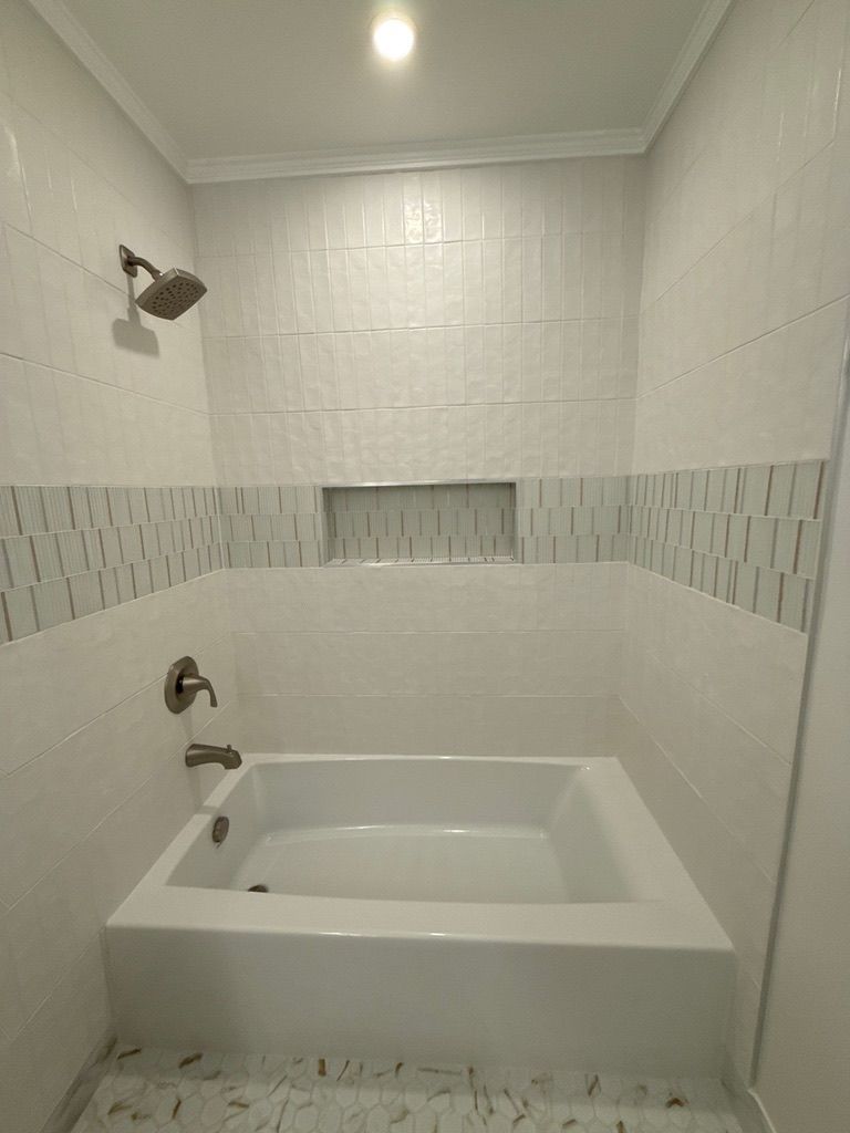 Small white tiled bathroom with a bathtub, shower head, and decorative tile band.