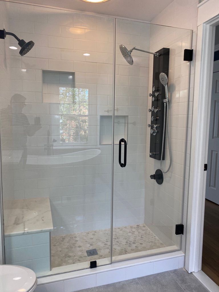 Modern glass shower with white tile, two showerheads, and built-in bench in a bright bathroom