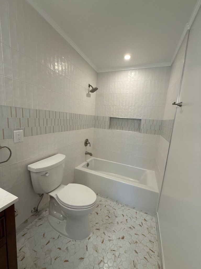 Small white bathroom with toilet, bathtub, tiled walls, and speckled floor.