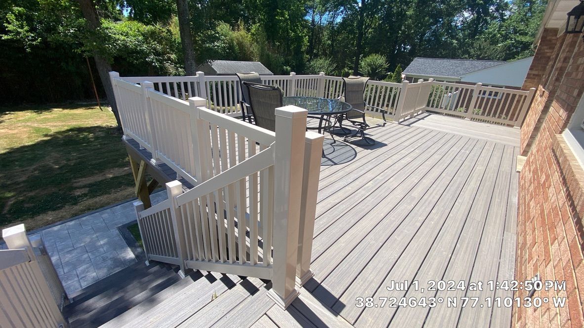 Backyard wooden deck with white railing and stairs, bordered by trees in sunlight