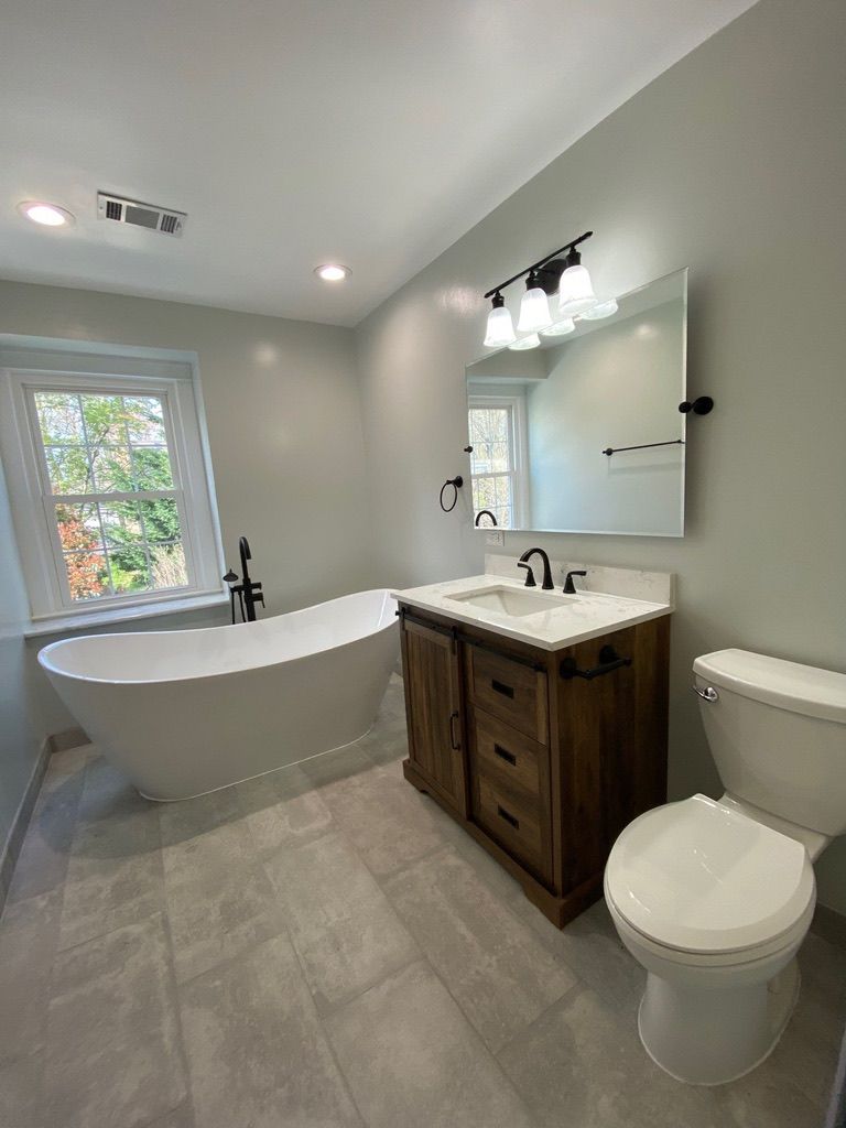 Bright bathroom with freestanding tub, vanity, toilet, and window, in light gray tones