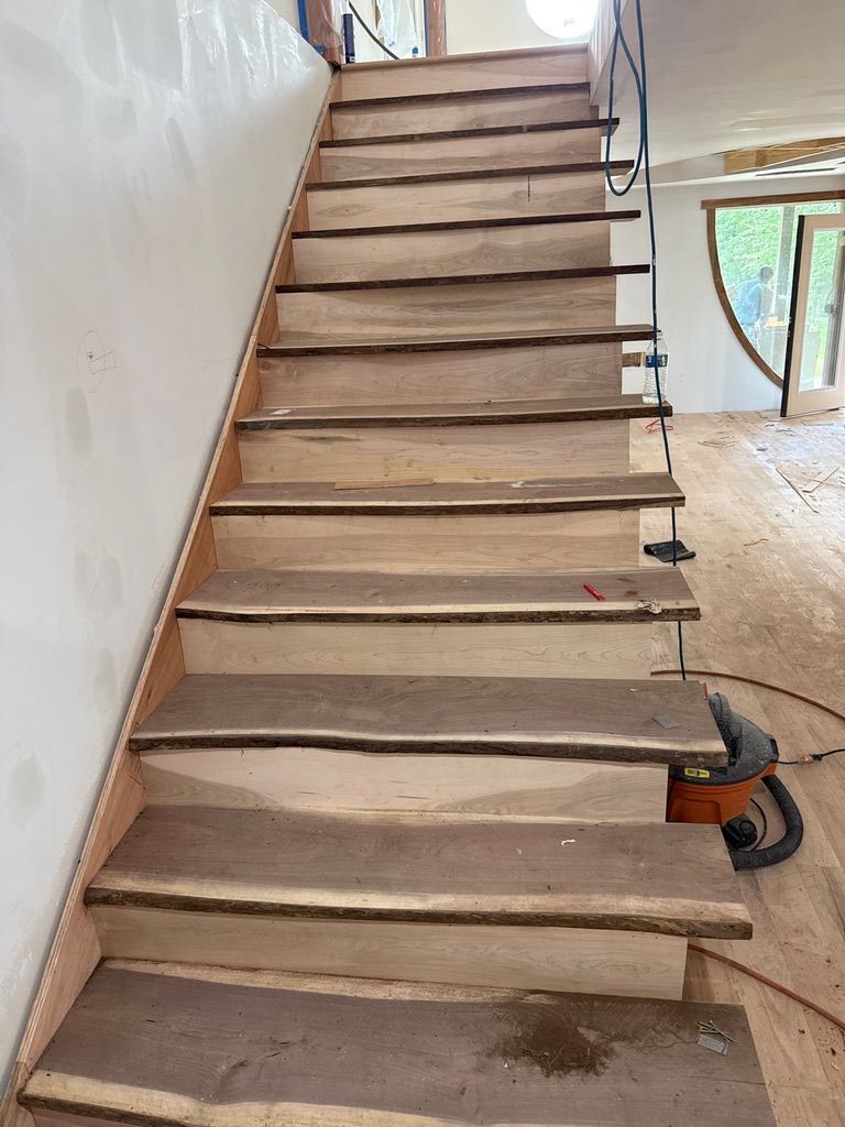 Unfinished indoor staircase with exposed wooden treads and drywall, viewed from the bottom.