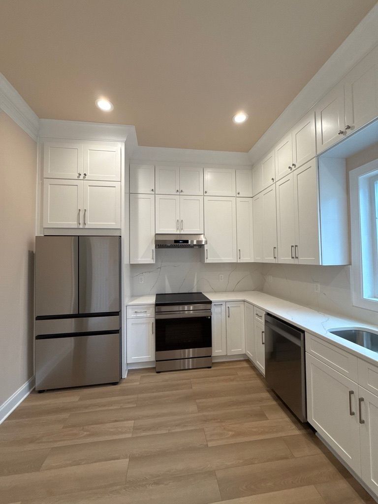 Bright white kitchen with stainless steel appliances, wood floor, and window over the sink.