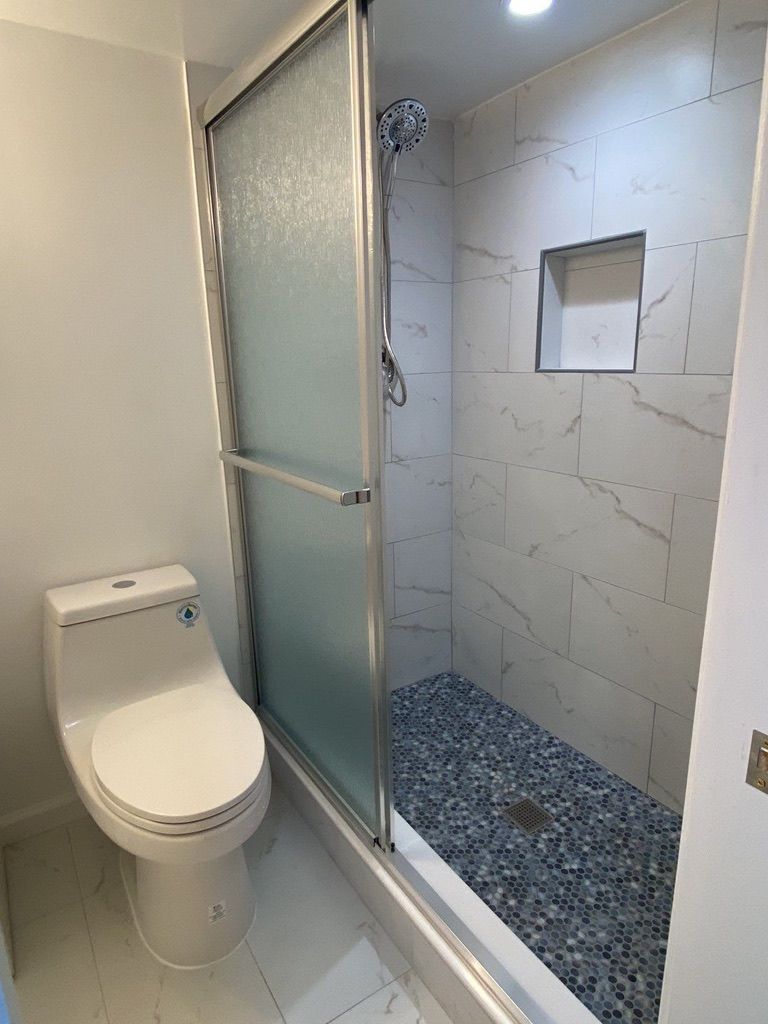 Accessible bathroom with a toilet and a frosted glass shower stall beside a pebble-floor wet room.