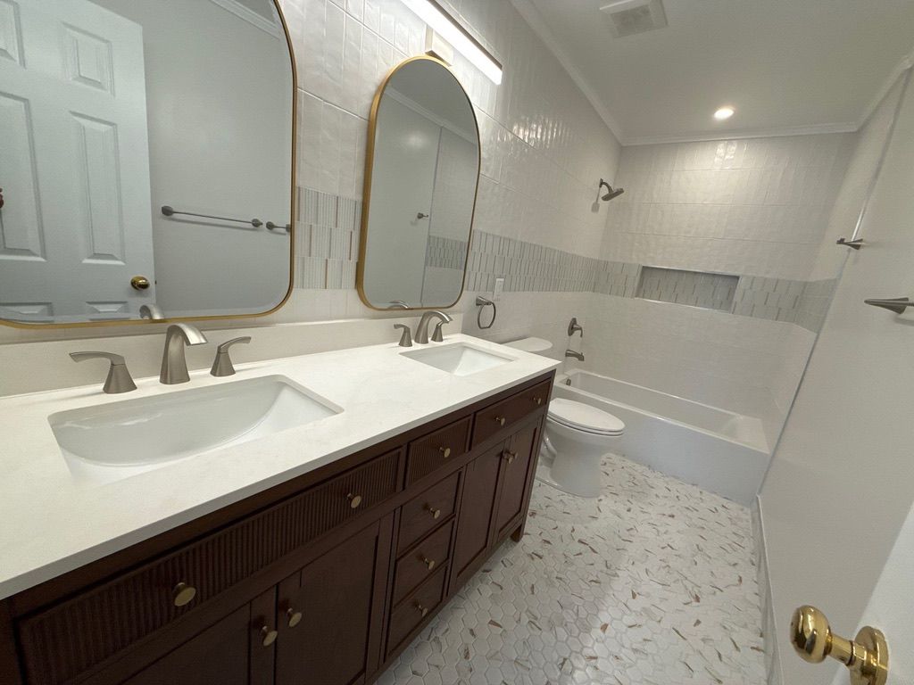 Bright bathroom with double vanity, gold mirrors, and a tiled walk-in shower.