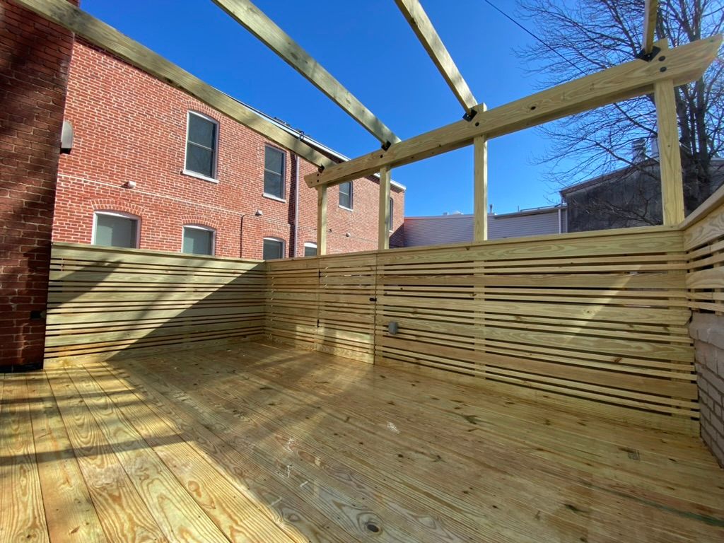 Wooden deck under construction beside a red brick building on a sunny day