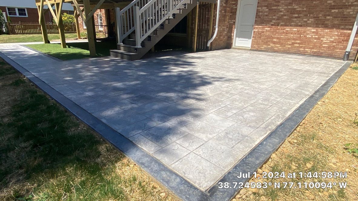 Concrete patio beside brick house with white stairs and a grassy edge in sunlight