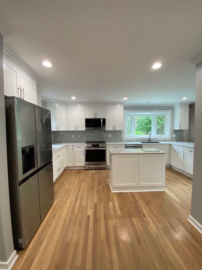 Bright modern kitchen with white cabinets, stainless appliances, island, and hardwood floors.