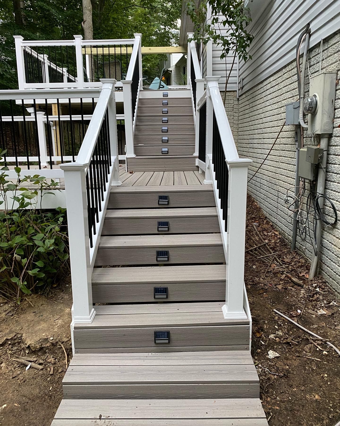 Wooden outdoor staircase with black step lights beside a house and deck railing