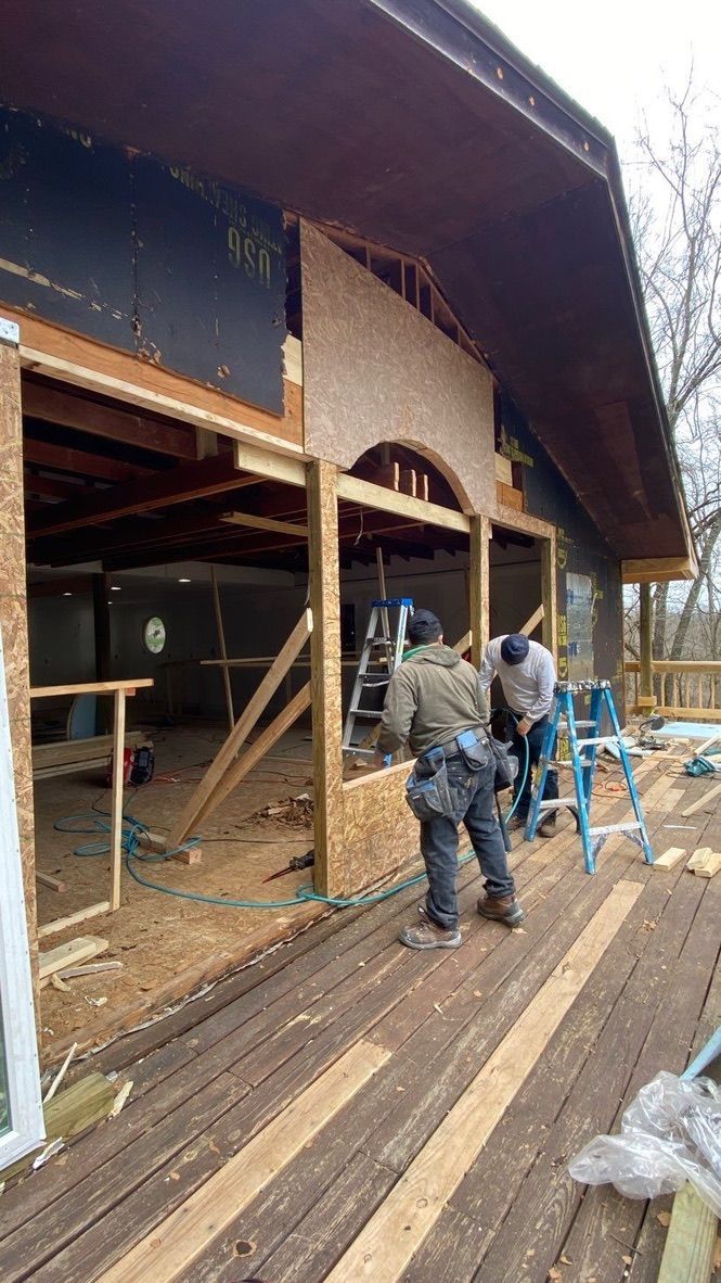 Workers installing siding on a house deck with ladders and exposed framing.