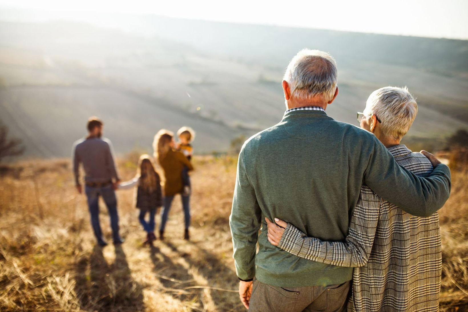 Couple embracing while overlooking a sunlit valley with a group walking ahead