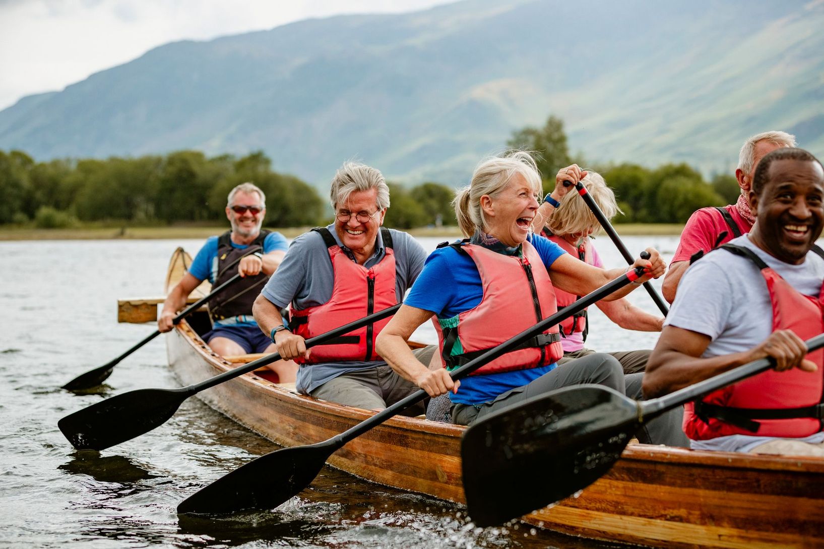 People paddling wooden canoes on a lake with mountains in the background