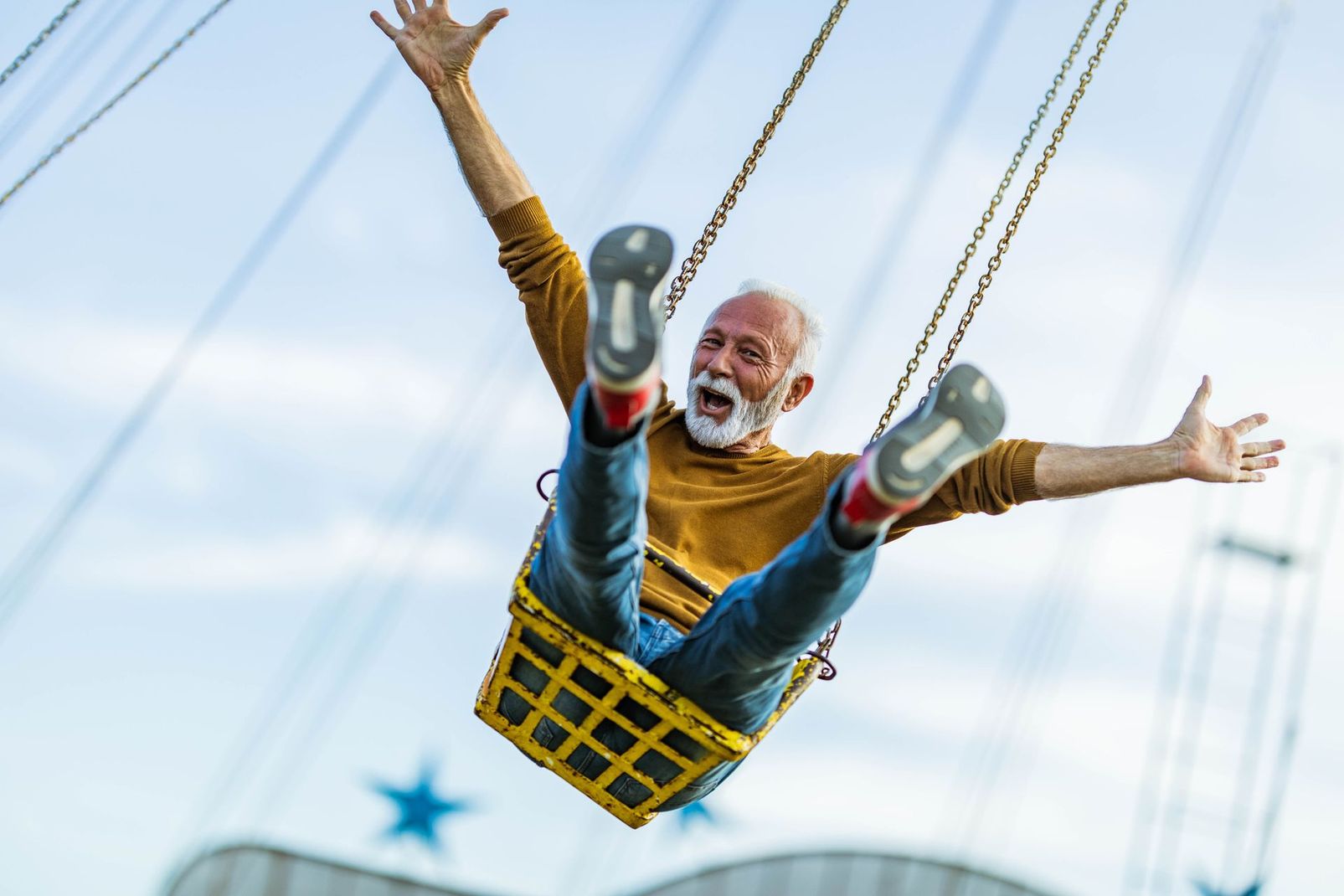 Man on a swing ride, legs up and arms wide against a bright sky
